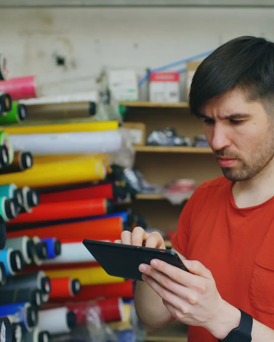 A print shop owner checking stock on a tablet among rolls of material